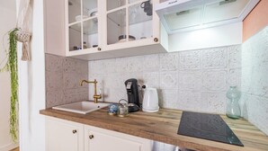 Cocina con armarios blancos, encimera de madera, un fregadero, cafetera y una planta decorativa de macramé.