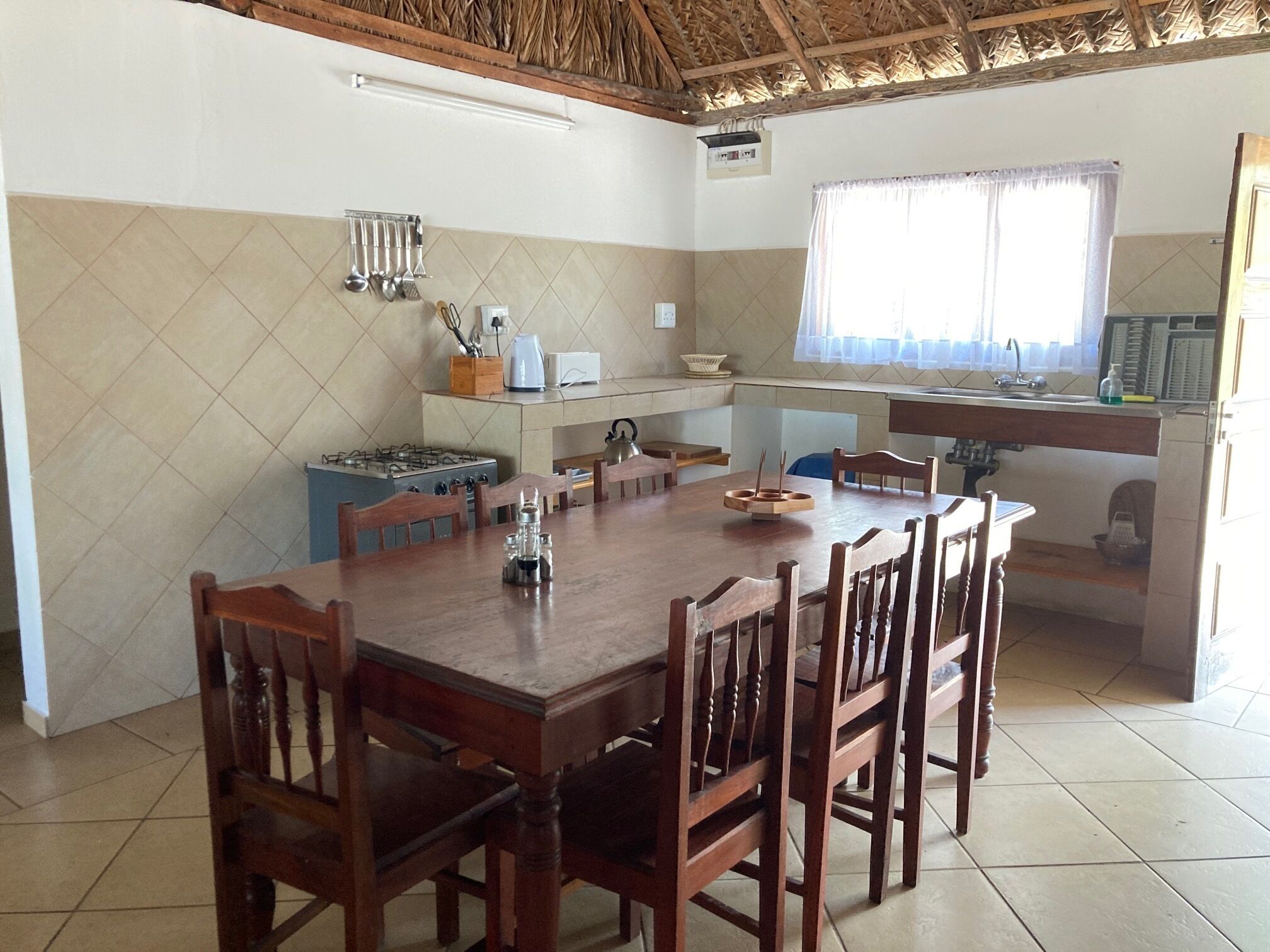 Uma sala de jantar com uma grande mesa de madeira, cadeiras, um fogão a gás e uma janela com cortinas.