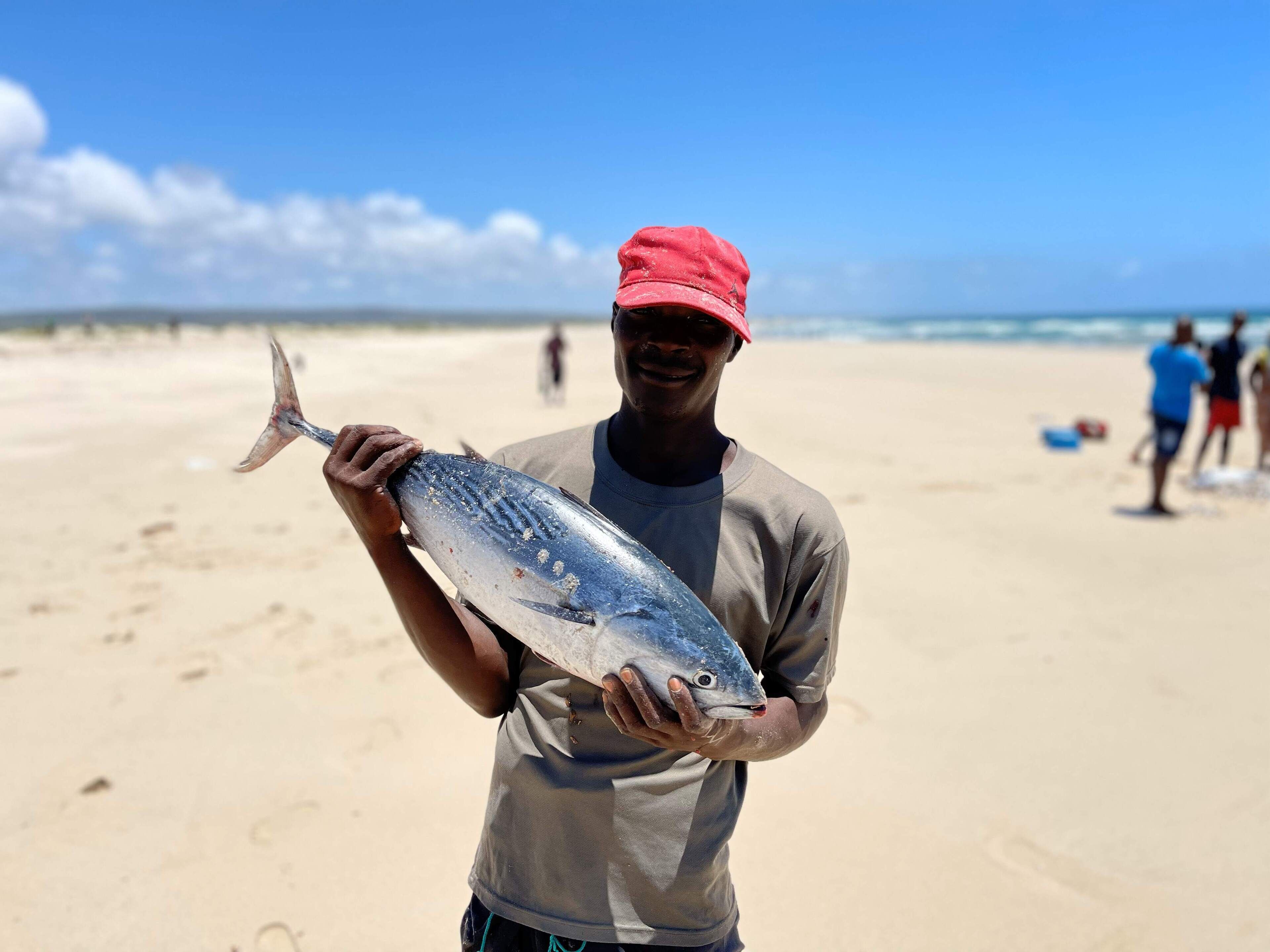 Una persona sosteniendo un pez en la playa.