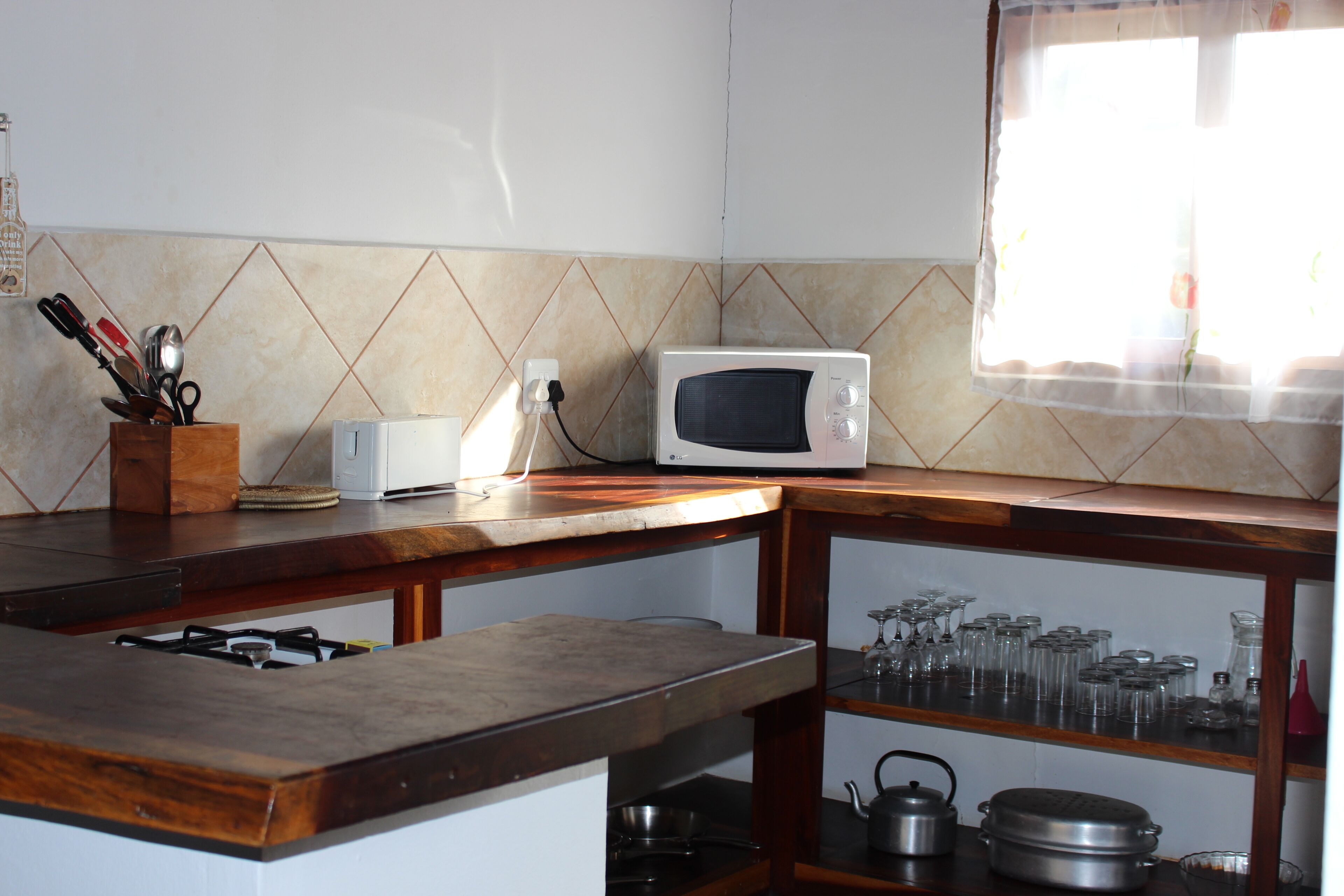 Une cuisine équipée d’un four à micro-ondes, d’une cuisinière à gaz et d’un plan de travail en bois. On y trouve des ustensiles rangés dans un bloc en bois et une étagère contenant de la vaisselle en verre.