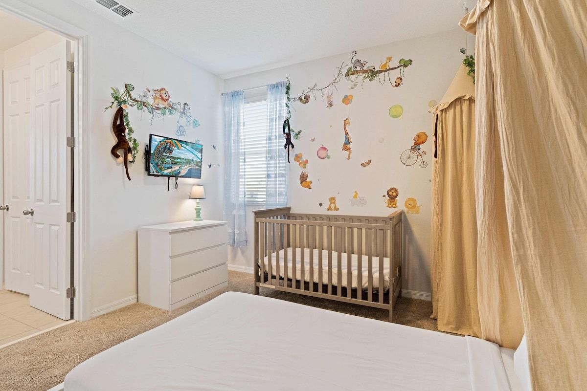 A bedroom with a crib, a dresser, a television, and a window with curtains.