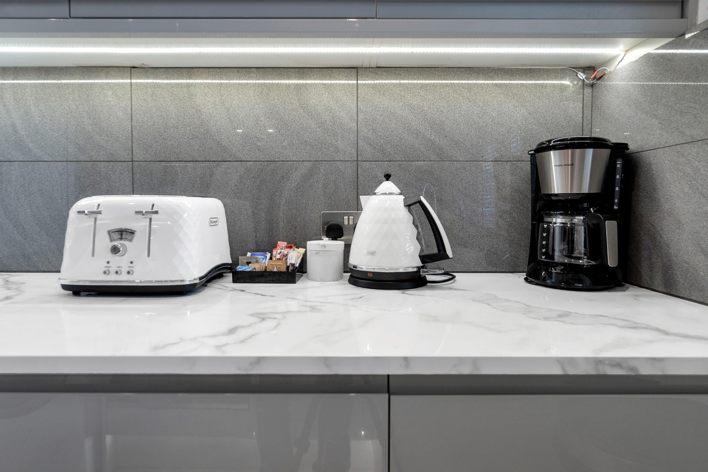 A kitchen with a coffee maker, toaster, and kettle on a marble countertop.