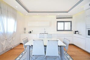 Eine moderne Küche mit weißen Schränken, einem Esstisch mit Stühlen und einem Fenster.