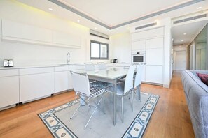 A modern kitchen with white cabinetry, a dining table with chairs, and a patterned rug.