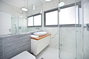 A modern bathroom with a glass shower enclosure, a white sink, and a marble-tiled vanity.