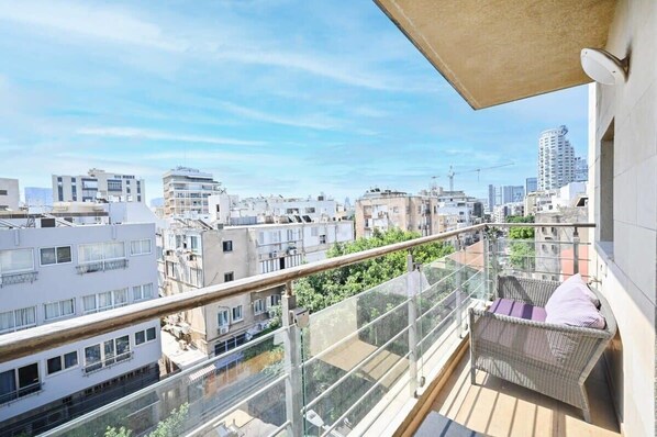 A balcony with a wicker chair and a view of a cityscape.