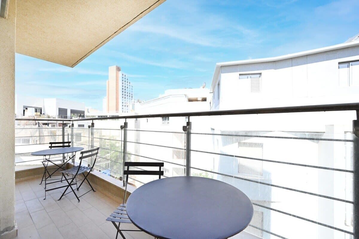 Ein Balkon mit Tisch und Stühlen, einer Glastrennwand und Blick auf Gebäude im Hintergrund.