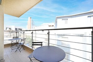 A balcony with a round table and two chairs, overlooking a cityscape with modern buildings.