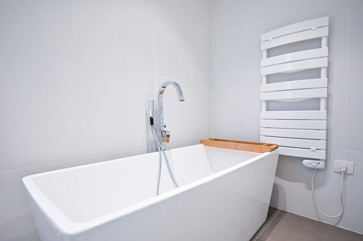 A modern bathroom with a freestanding bathtub, a wall-mounted towel rack, and a wooden shelf.