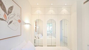 Een slaapkamer met een groot bed, een garderobe met spiegeldeuren en een kunstwerk aan de muur.