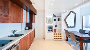 A modern kitchen with wooden cabinets, a built-in oven, and a dining area with a table and chairs. - One step to the Sea by HolyGuest (Tel Aviv)