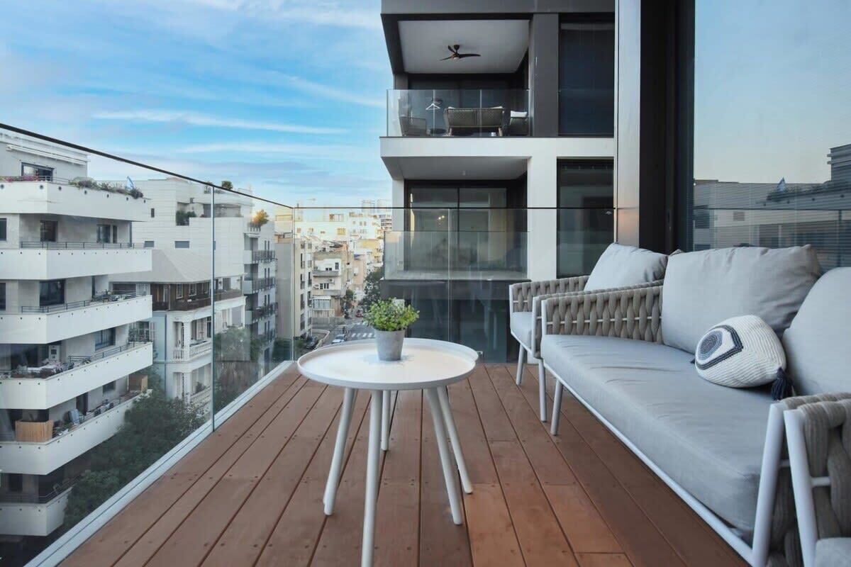 Ein moderner Balkon mit Holzboden, einem runden Tisch mit einer Pflanze und einer Couch mit Kissen.