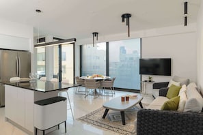 Una cocina moderna con una isla central, comedor con sillas, un sofá y un televisor.