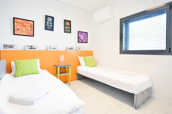 A hotel room with two beds, a small table, and a window with blinds.