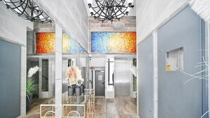 Eine moderne Hotelhalle mit einer zentralen Sitzgruppe, einer Treppe und einer farbenfrohen Mosaikwand.