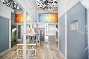 A modern hotel lobby with a central seating area, a staircase, and a colorful mosaic wall.