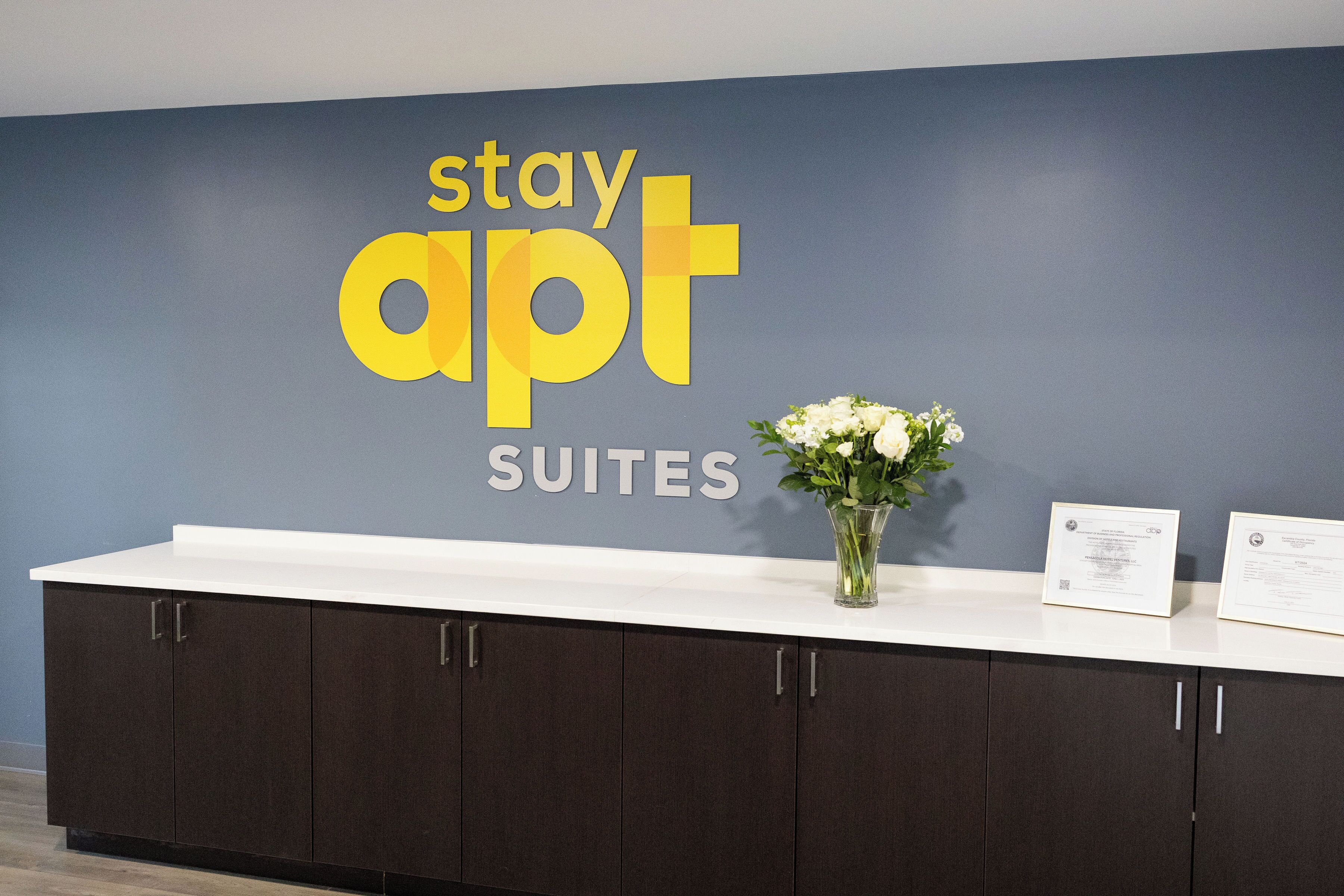 A reception desk with a blue wall, a white counter, and dark cabinets. There is a vase with white flowers on the counter.