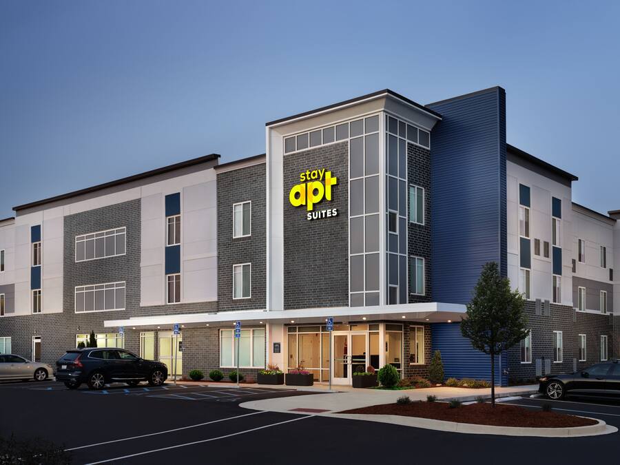 Een modern hotel met een bord waarop 'apt suites' staat, en een parkeerplaats met auto's.