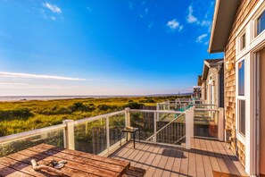 A wooden deck with a glass balustrade overlooking a beach and grassy dunes. - Beach Dream One in Moclips (Moclips)
