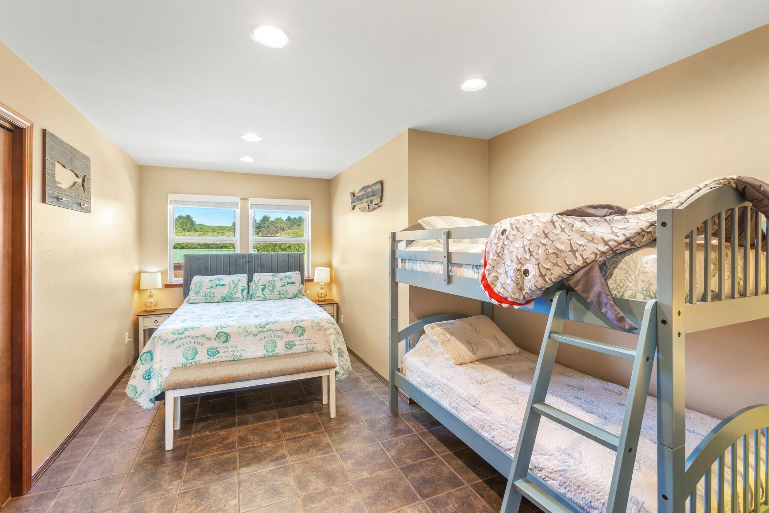 A bedroom with a bunk bed, a single bed, and a window with a view of greenery.