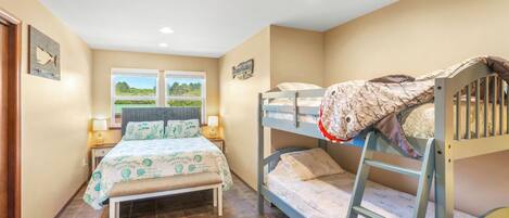 A bedroom with a bunk bed, a single bed, and a window with a view of greenery.