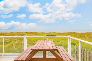 Ein Holztisch für ein Picknick auf einer Terrasse mit Blick auf den Strand und grüne Dünen.