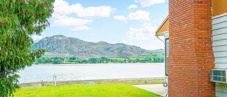 A house with a brick exterior, a grassy yard, and a view of a lake with mountains in the background.