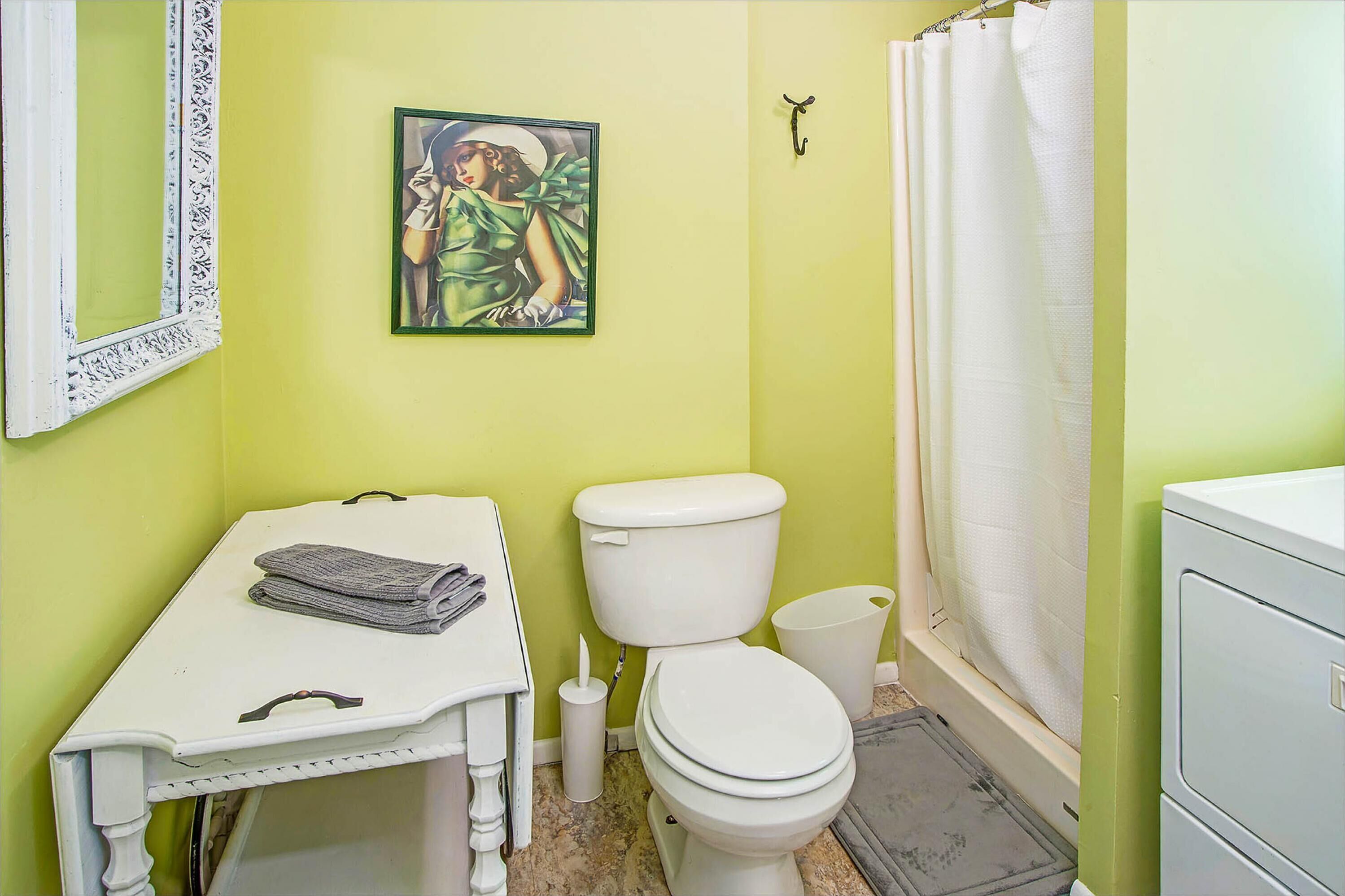 A bathroom with a toilet, a sink with a towel, a framed picture on the wall, and a shower curtain.