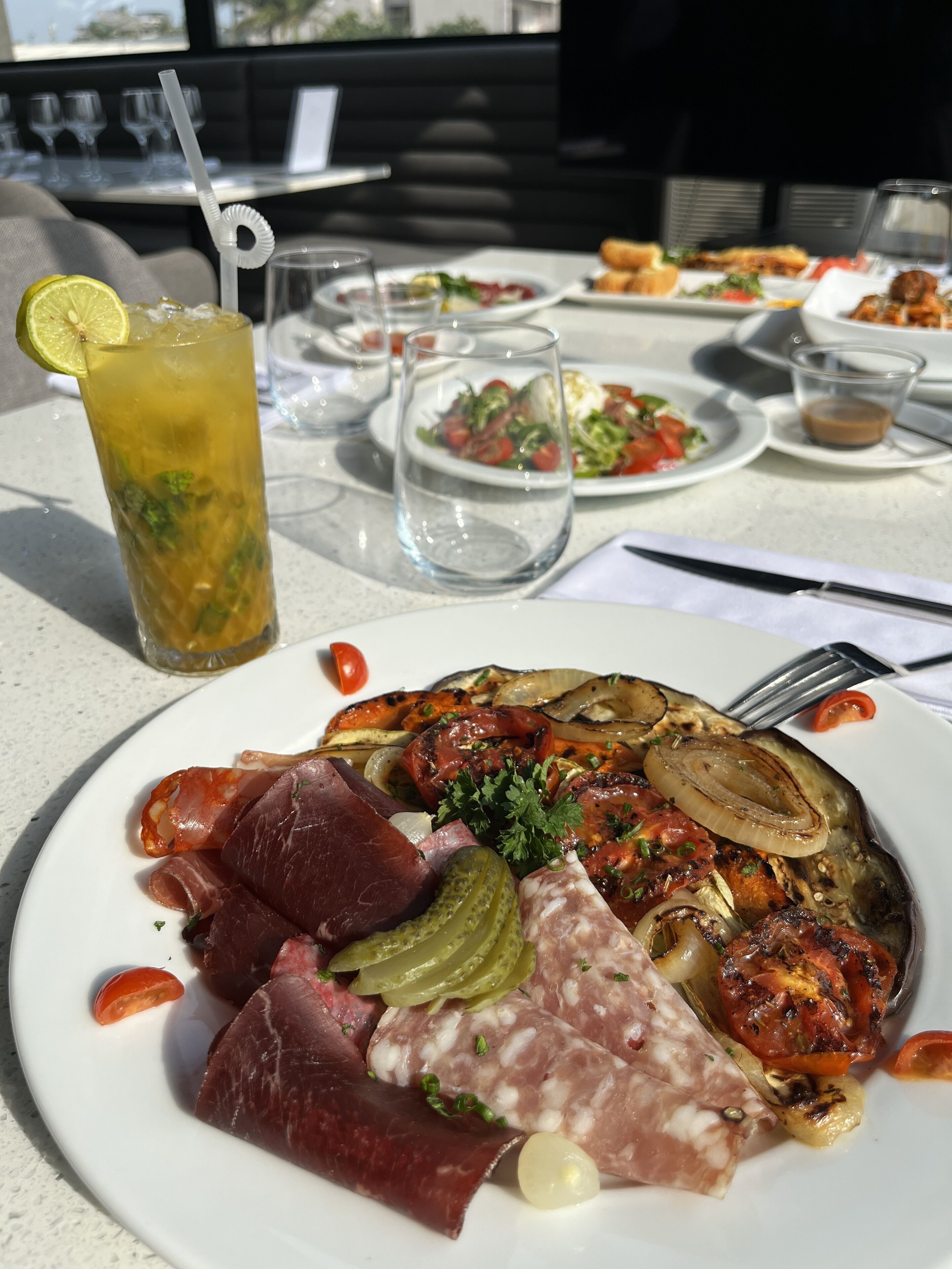 A dining table with plates of food, a drink, and glasses.