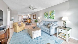 A living room with a sofa, coffee table, TV, and a dining area in the background.