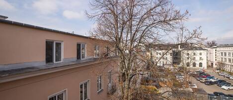Un edificio de varios pisos con balcones, un estacionamiento y un árbol en primer plano.