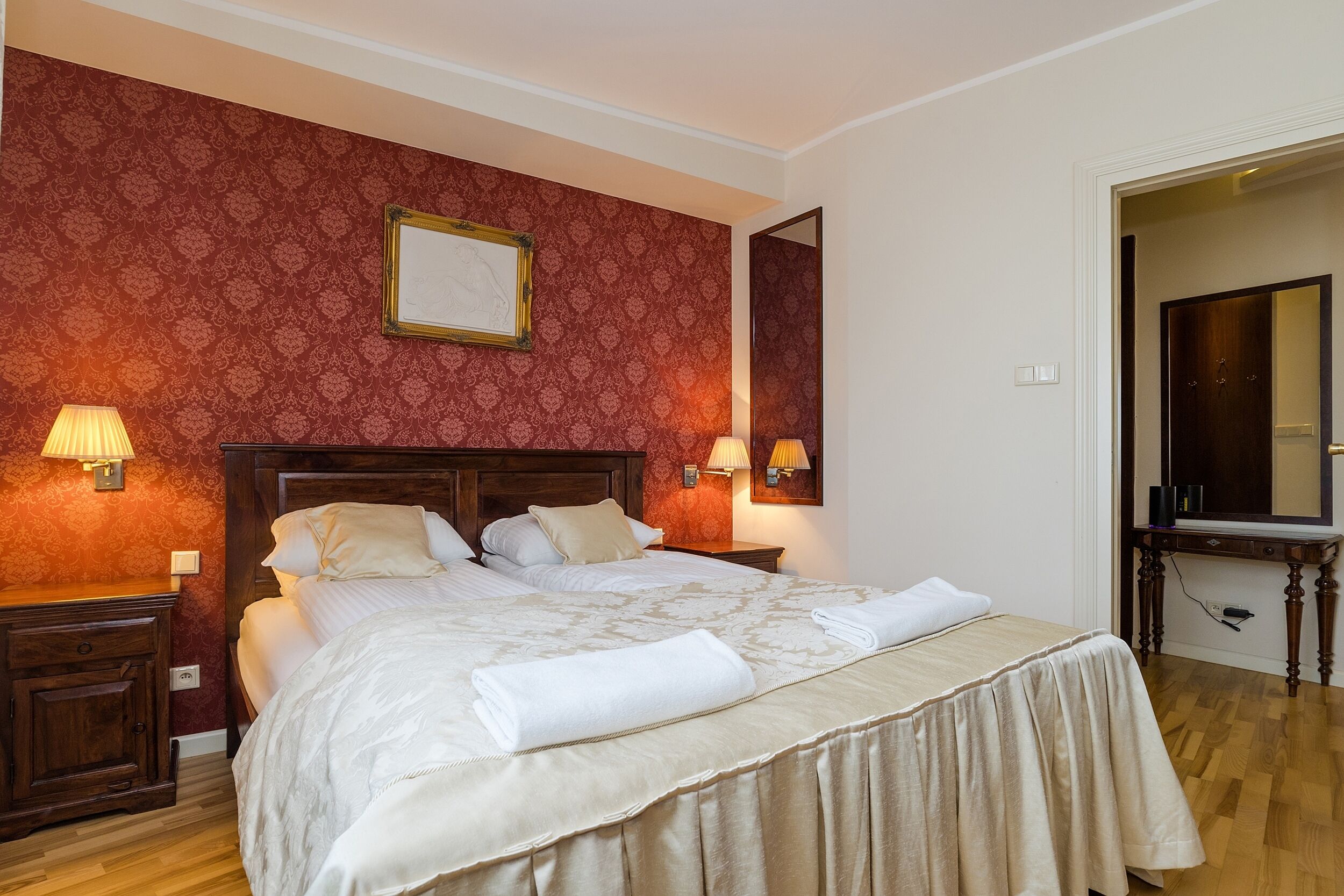 A neatly made bed with a wooden headboard, two bedside tables with lamps, and a mirror above the bed.