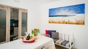 A dining area with a table set for two, a bench, and a painting of a beach scene. - Perle Del Mare - Perla a 70m Dalla Spiaggia Maldive del Salento Area (Salve)