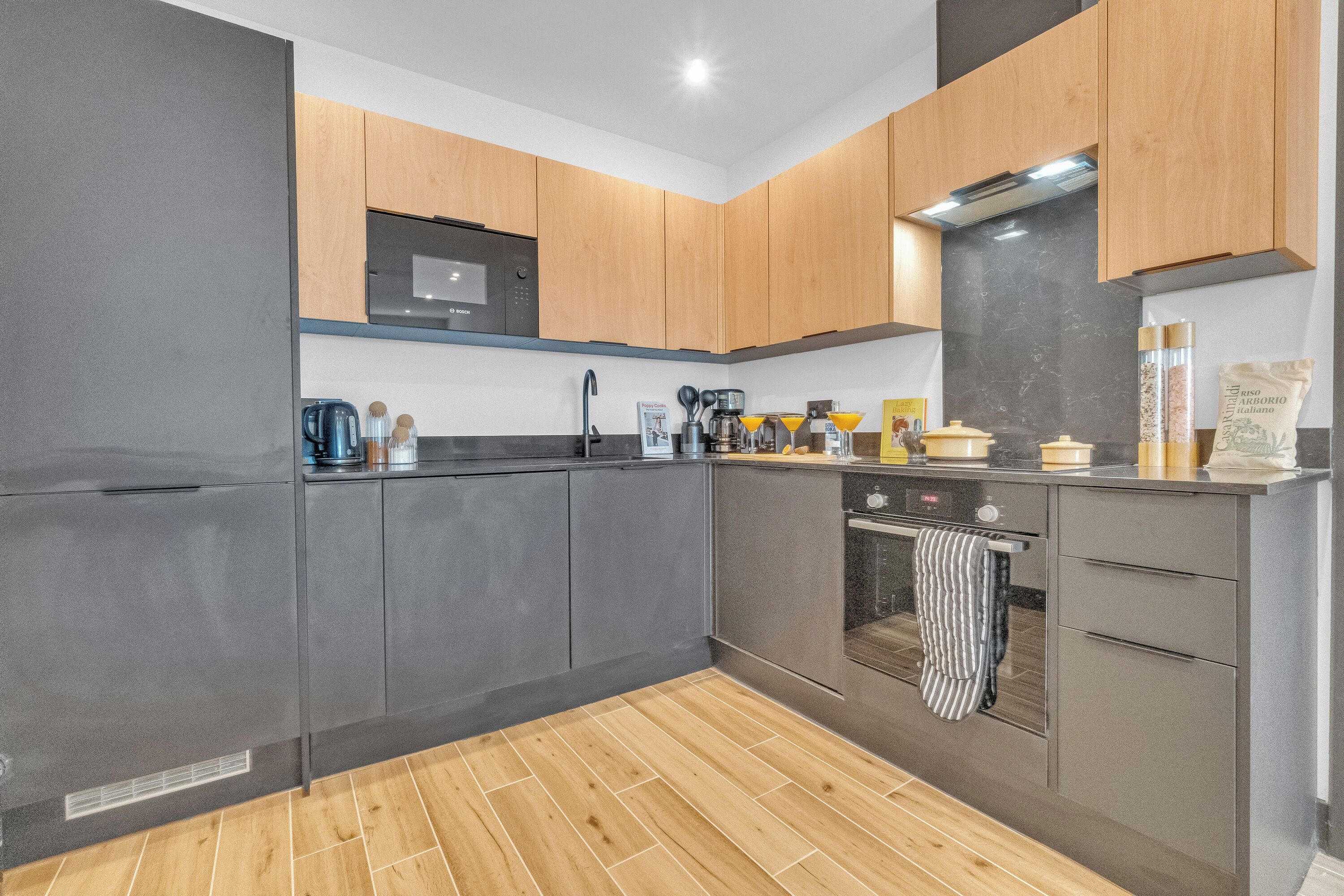 A modern kitchen with grey cabinets, a black countertop, and a wooden floor.