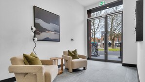 A modern lobby with a sofa and armchair, a small wooden table, and a large abstract painting. - homely - Luxury Apartments Finchley (London)