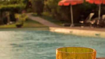 A glass on a wooden surface with a pool and a building in the background.