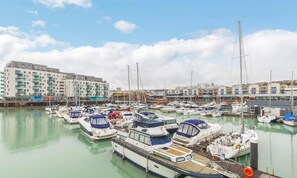 A marina with multiple boats docked, a large building with balconies, and a clear sky.