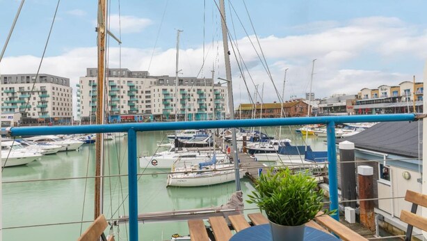A marina with multiple boats docked, a balcony with a potted plant, and buildings in the background. - On the Water -waterside Studio With Terrace Overlooking the Harbour (Brighton)