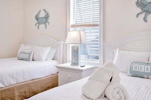 A bedroom with two beds, a nightstand, a lamp, and decorative starfish and crab wall art.