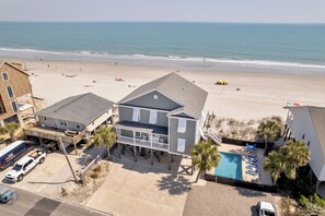 A beachfront property with a pool, a covered deck, and a beach view.