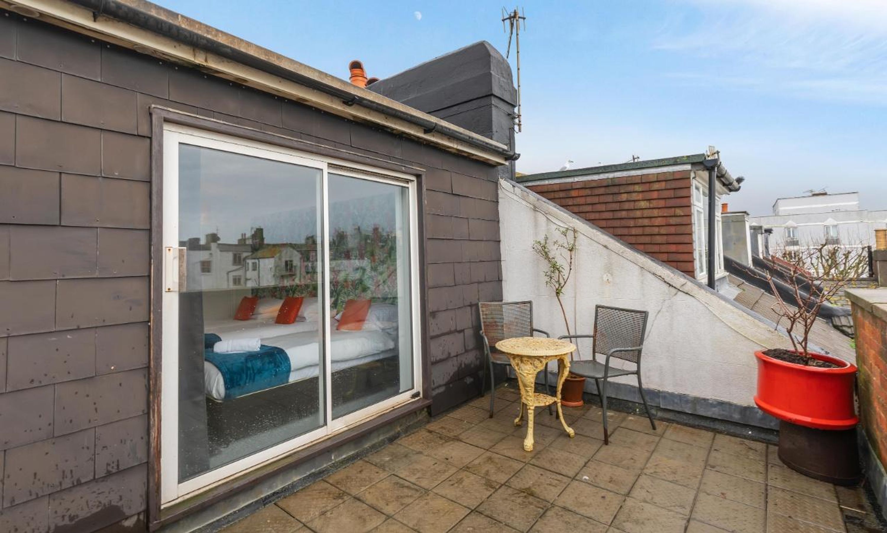 A small balcony with a bed, a table, and chairs.