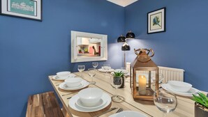 A dining area with a blue wall, a framed picture of a building, a table set with white plates and glasses, and a lit candle in a lantern. - Seabright Townhouse- Super Stylish House- Parking for one Car- Sleeps up to 12 (Brighton)