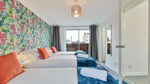 A hotel room with two beds, a tropical wallpaper, a city view, and a modern light fixture. - Seabright Townhouse- Super Stylish House- Parking for one Car- Sleeps up to 12 (Brighton)