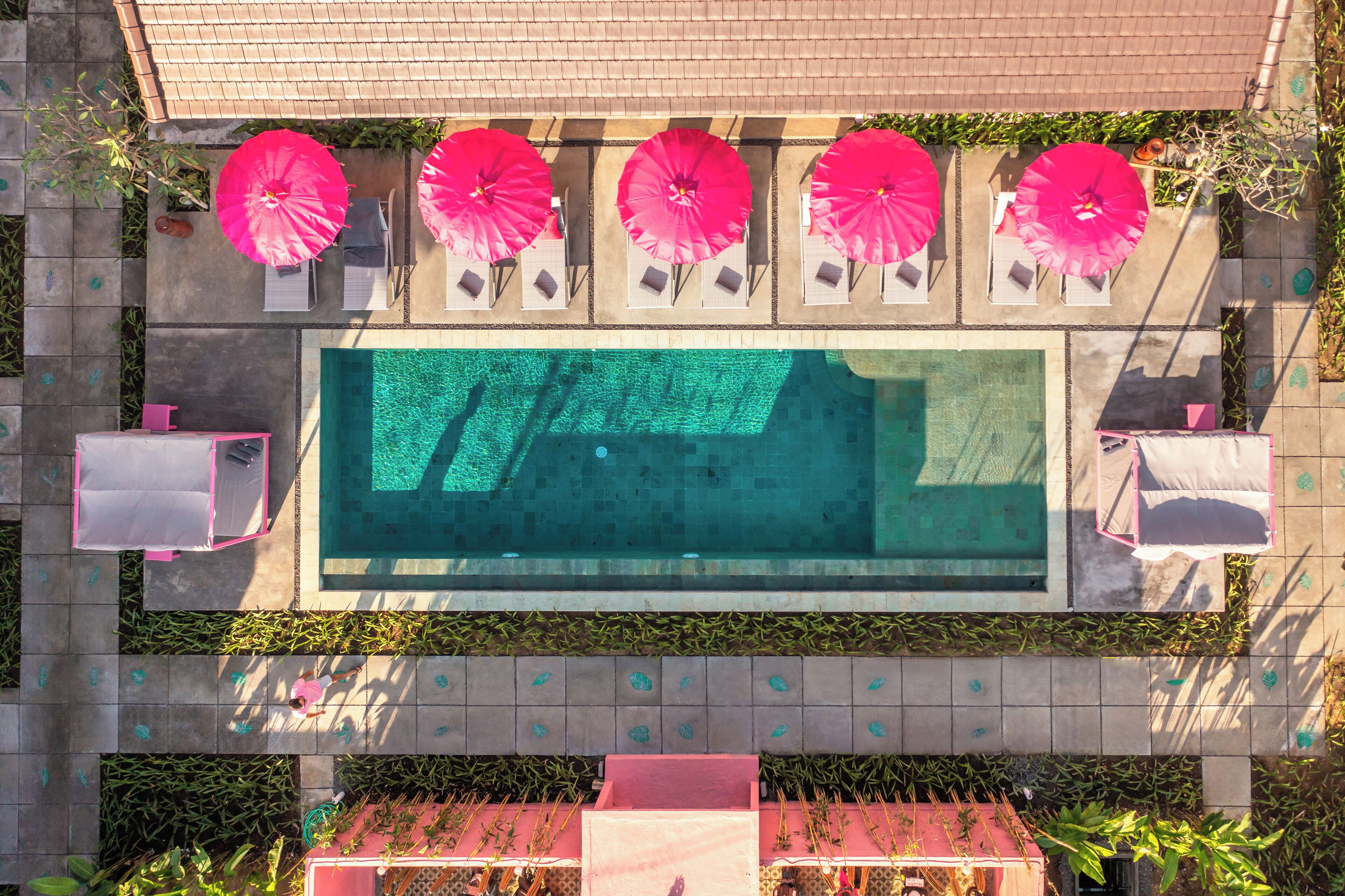 Vue aérienne d’un espace piscine avec plusieurs chaises longues et parasols.