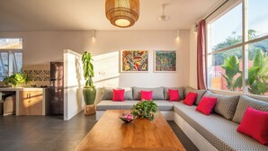 A modern living room with a wooden coffee table, a sofa with patterned cushions, and a large window with a view of greenery. - PinkPrivate Balangan - for Cool Adults Only (Jimbaran)