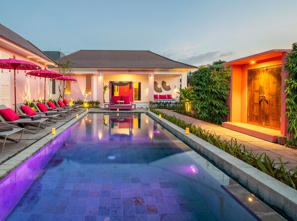 A swimming pool with lounge chairs and umbrellas, a covered seating area, and a wooden door. - PinkPrivate Balangan - for Cool Adults Only (Jimbaran)