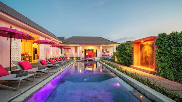 A swimming pool with lounge chairs and umbrellas, surrounded by greenery and a building with a red door. - PinkPrivate Balangan - for Cool Adults Only (Jimbaran)