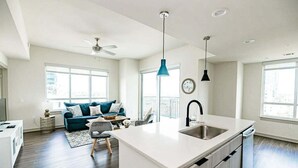 A modern kitchen with a central island, a dining area with a blue sofa, and large windows providing natural light.