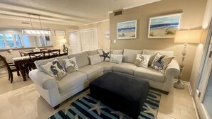A living room with a sectional sofa, a dining table, and chairs. There is a starfish-patterned rug on the floor. - 21c Richmond Park 3 Bedroom Villa (Myrtle Beach)