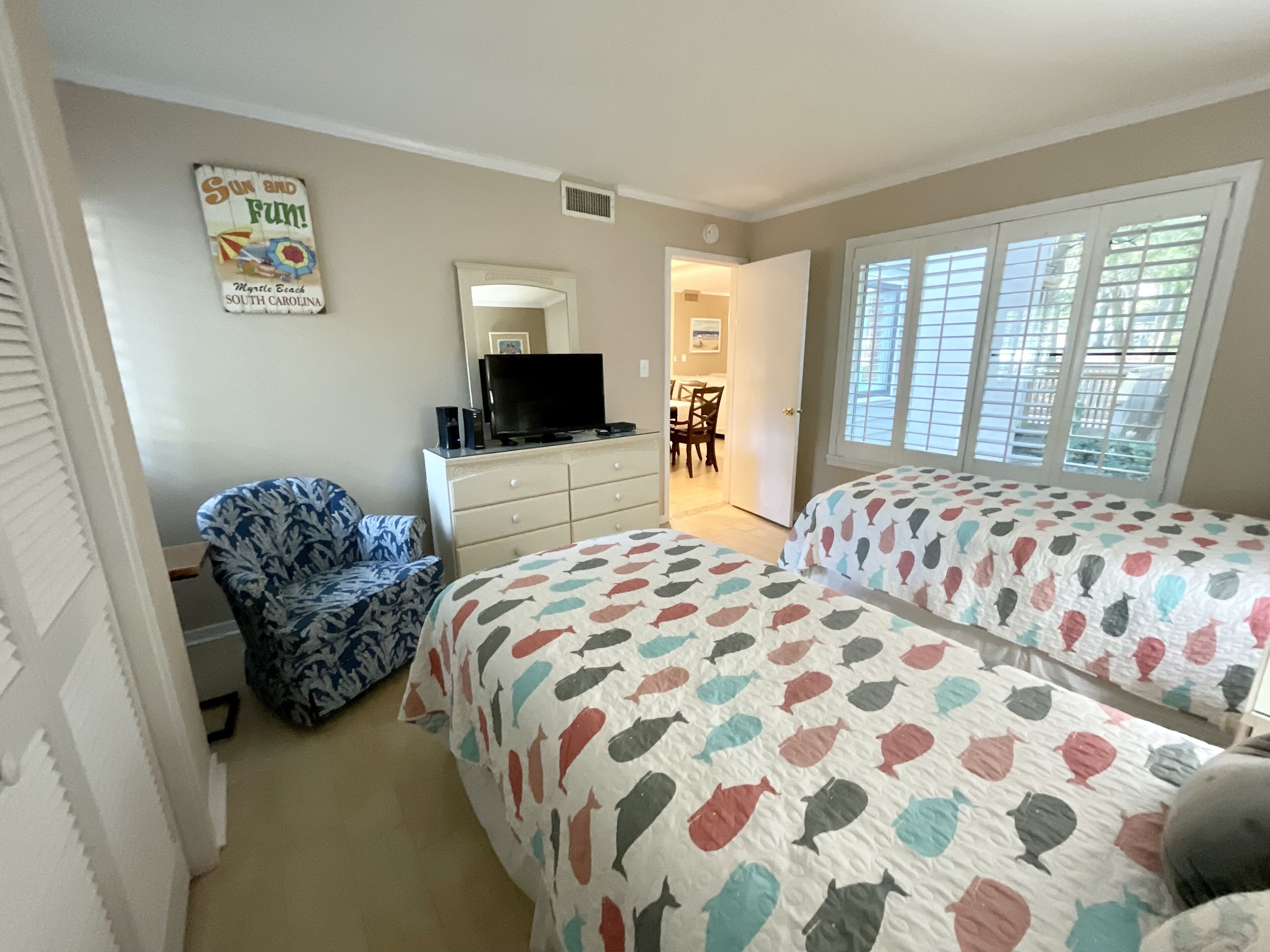 Un dormitorio con dos camas, un aparador, una televisión y una silla.